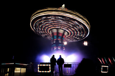 Low angle view of silhouette people at amusement park against sky at night