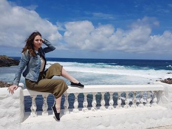 Young woman sitting on railing against sea at beach