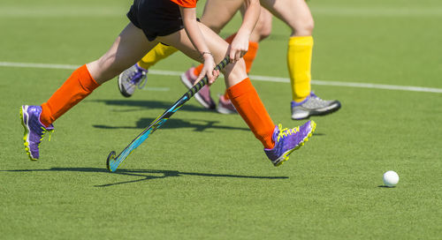 Low section of people playing soccer ball on grass