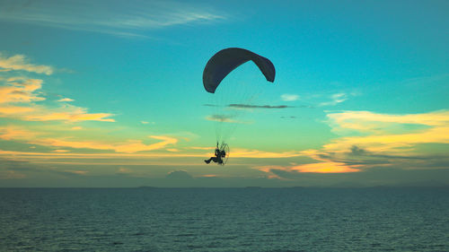 Person paragliding over sea against sky during sunset