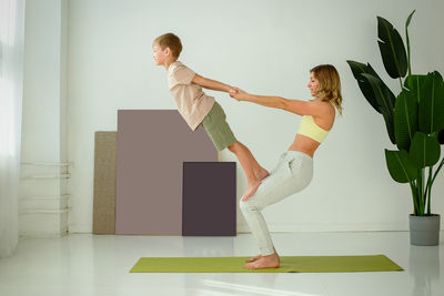 A woman, doing yoga with a child boy, doing exercises with support.