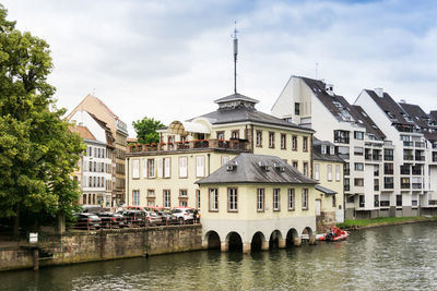 Buildings by river in city against sky