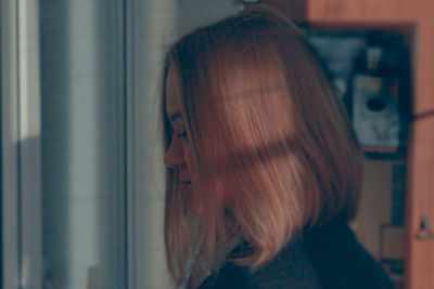 Portrait of young woman looking through window at home