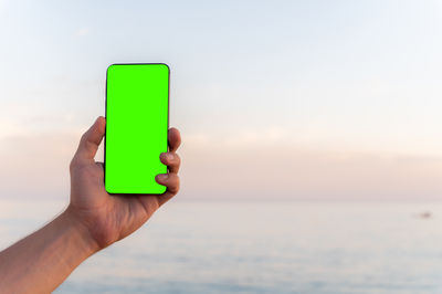 Cropped hand of woman holding mobile phone at beach