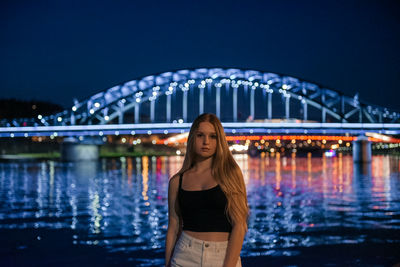 Portrait of young woman standing against river at night