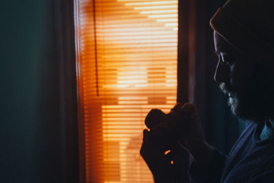 Side view of man standing against window at home