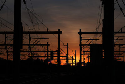 Silhouette electricity pylon by railroad tracks against sky during sunset