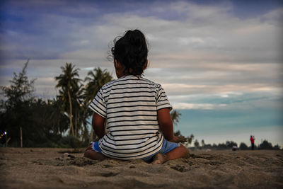 Rear view of woman sitting on land against sky