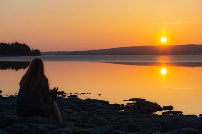 Rear view of woman sitting on beach during sunset