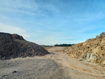 Dirt road amidst land against sky