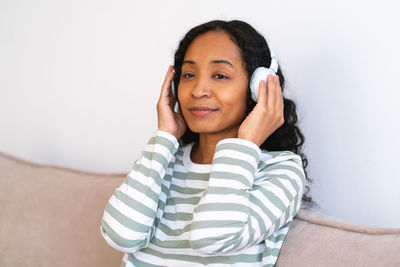 Enjoying music in headphones. delightful african-american female listening to symphony on couch