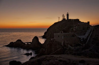 Lighthouse by sea against sky during sunset