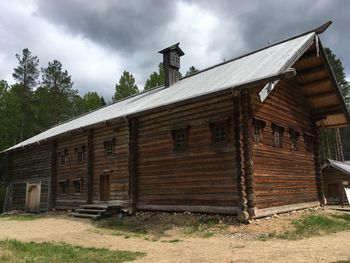 Old wooden house on field by building against sky