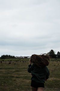 Rear view of woman walking on field against sky