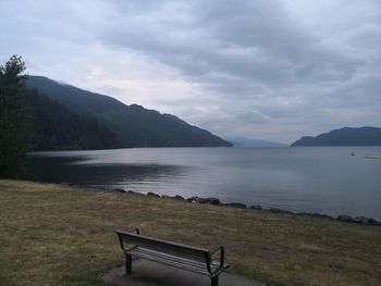 Empty bench by lake against sky