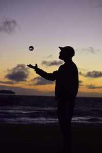 Silhouette man playing with crystal ball on beach against sky during sunset