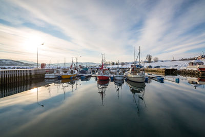 Boats in harbor against cloudy sky