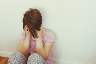 Sad woman sitting on floor against wall