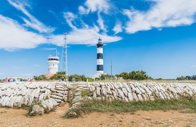 Lighthouse on field by building against sky