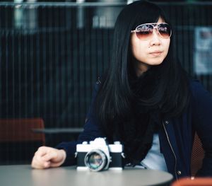 Young woman in sunglasses with camera sitting on chair