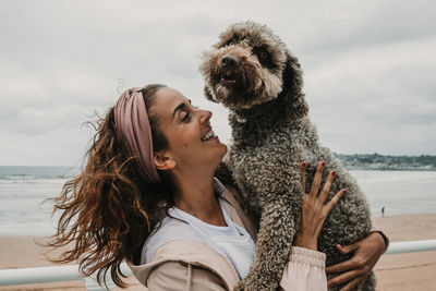 Smiling woman carrying dog while standing at beach