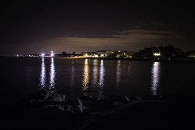 Illuminated city by river against sky at night