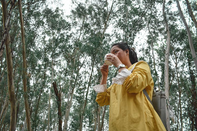 Low angle view of woman standing in forest while drinking