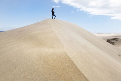 Man on sand dune in desert against sky