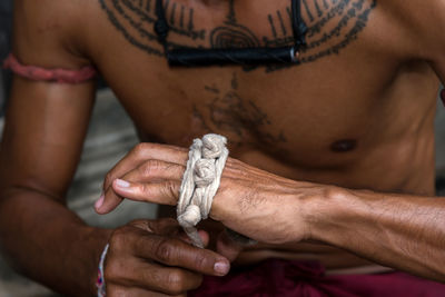 Midsection of shirtless man wrapping textile on hand