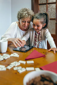 Girl with grandmother using digital tablet on table at home