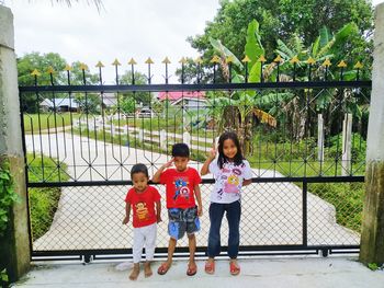 Children standing by fence against sky