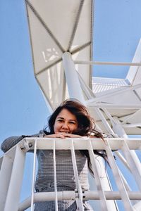 Low angle portrait of young woman standing by railing