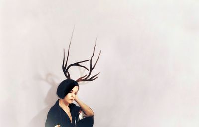 Contemplating woman with artificial antler standing against wall