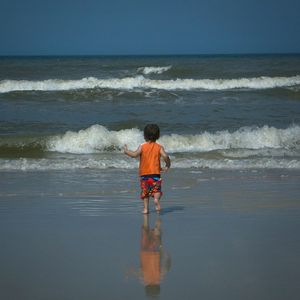 Rear view of man standing at beach against sky