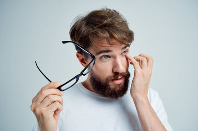 Young man holding eyeglasses against white background