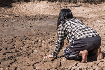 Rear view of woman kneeling on barren land