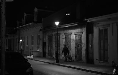 Rear view of man walking on illuminated street amidst buildings at night
