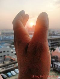 Close-up of hand against sea during sunset