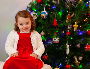 Portrait of cute girl sitting by christmas tree at home