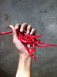 Cropped hand holding red chili pepper on table