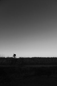 Silhouette person riding bicycle on field against clear sky