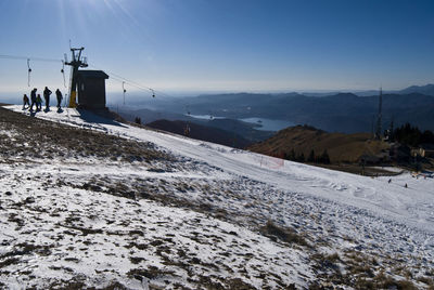 People standing by overhead cable car on snowcapped mountain