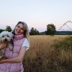 Young woman with dog standing on field against sky