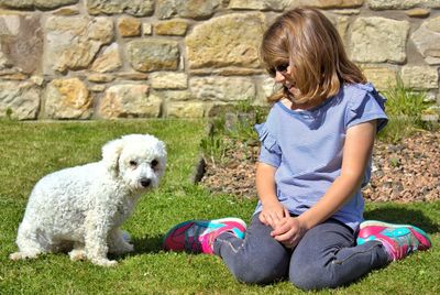 Girl sitting with dog on grassy field