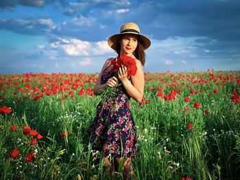 Woman standing by poppy flowers on field against sky