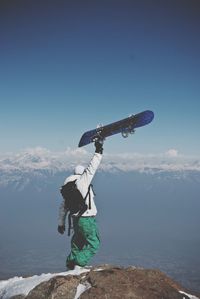 Rear view of man holding skateboard while standing on mountain against sky