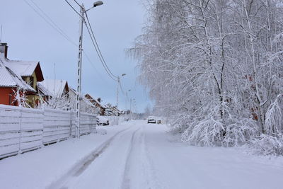Snow covered road amidst trees and houses during winter