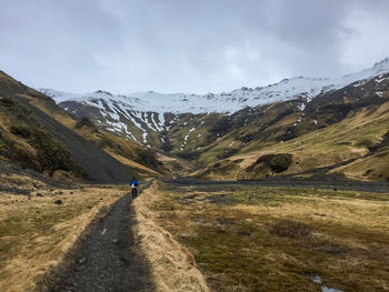 Man walking on road amidst snowcapped mountains against sky