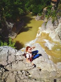 High angle view of woman sitting on rocks by waterfall