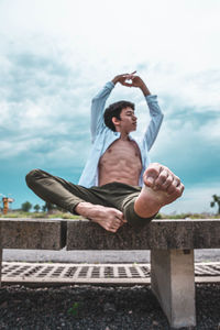 Full length of young man sitting against sky